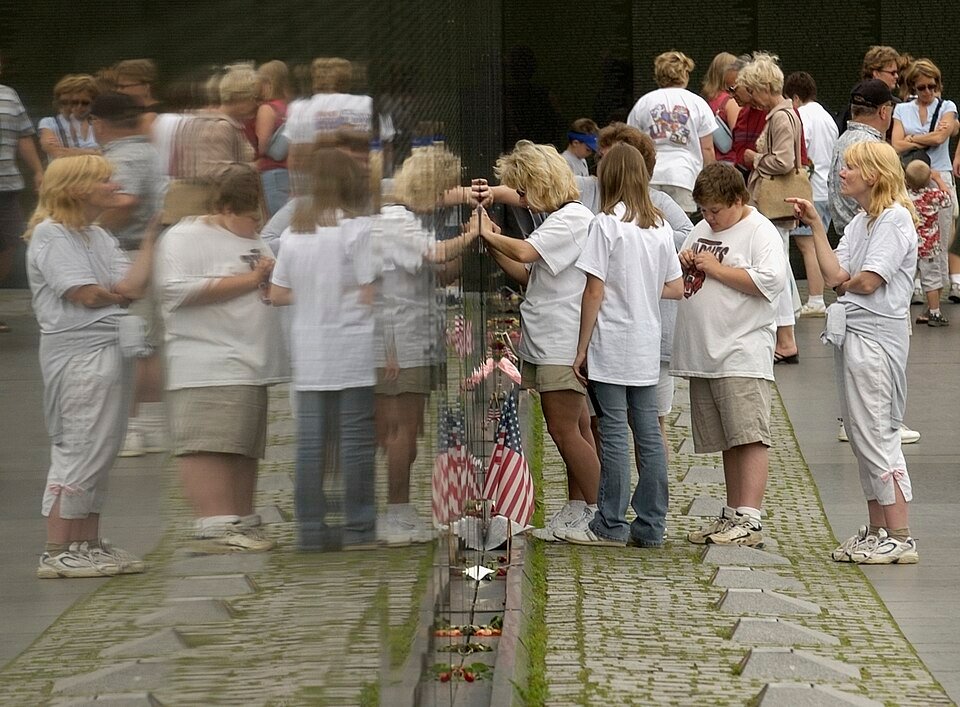Visitors taking pencil rubbings of names on the black granite Vietnam Veterans Memorial wall